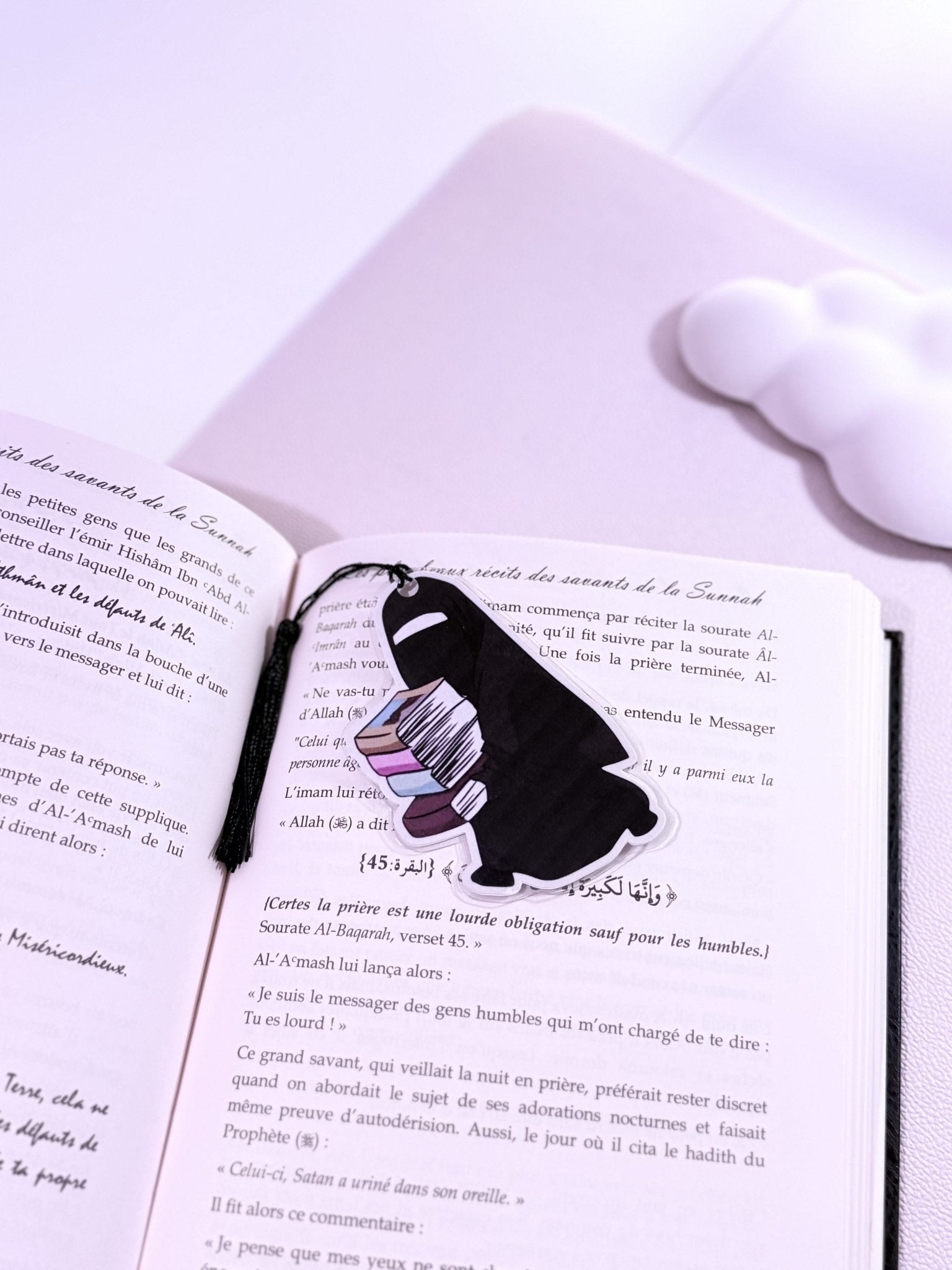 Un marque page d'une fille en niqab , qui tient  des livres dans ses main , posé sur un livre ouvert