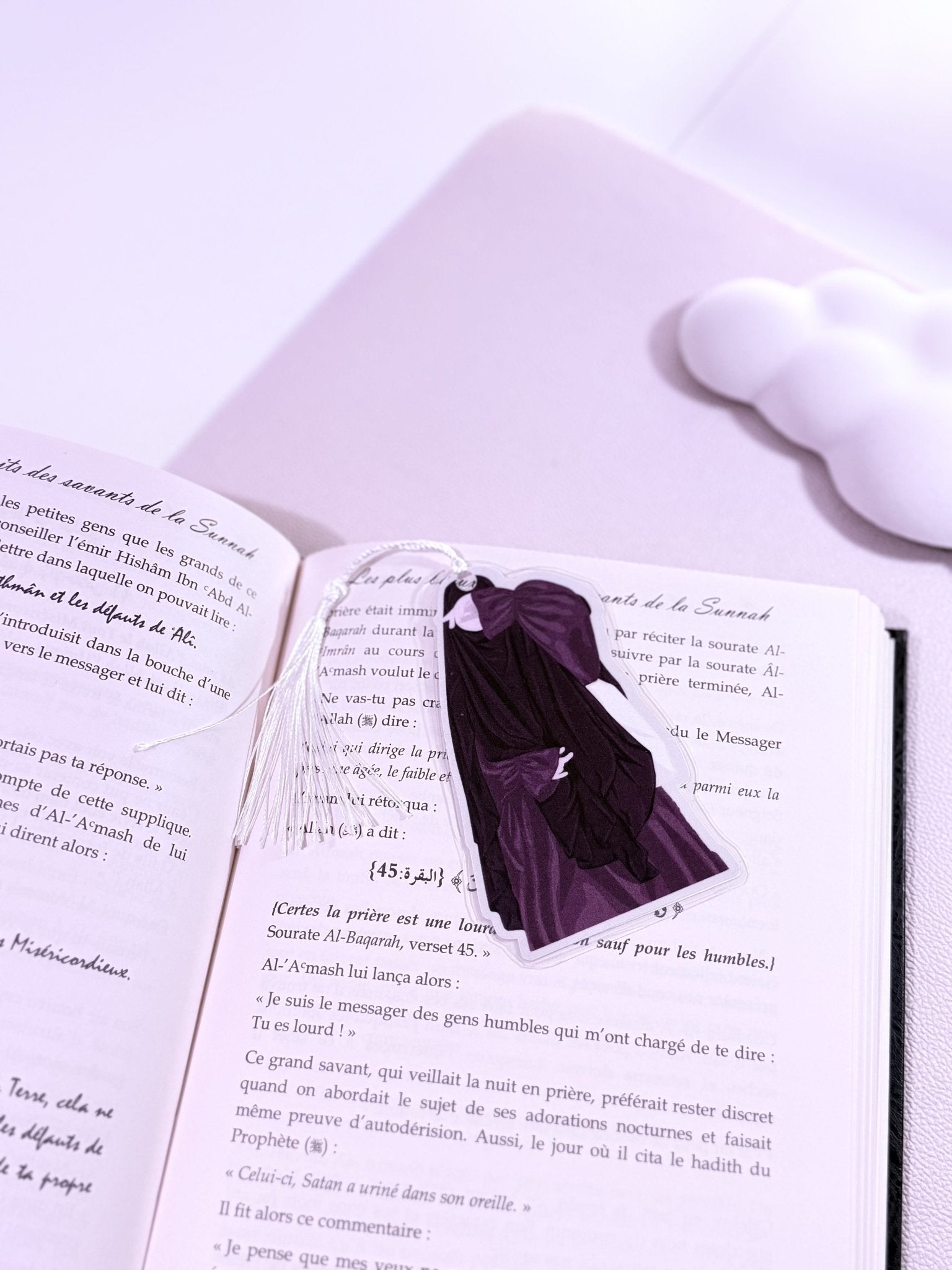 Un marque page d'une fille en niqab habillé en noir et couleur prune posé sur un livre ouvert