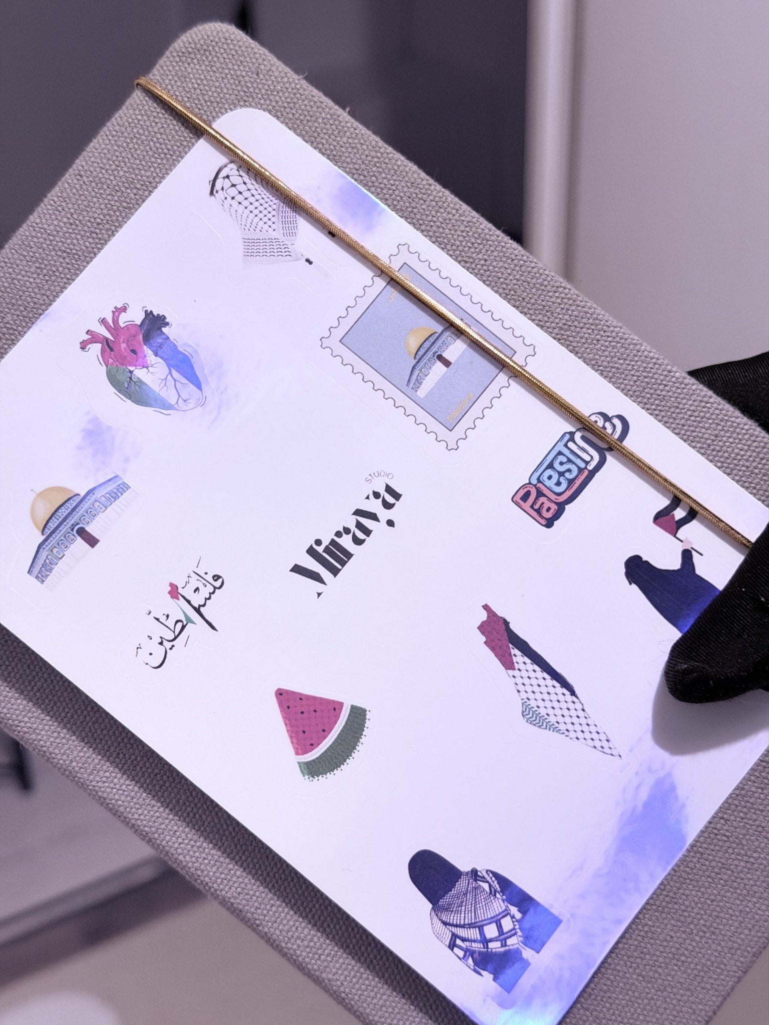 Une main qui présente une Feuille de 10 pack de stickers motif palestine posé sur un cahier