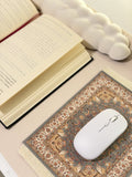 Un tapis de souris orieltal couleur rose claire posé sur un bureau avec un livre ouvert